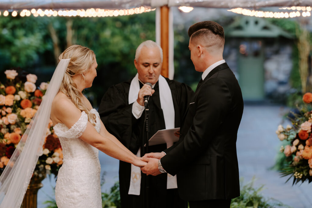 Bride and groom hold hands during their wedding ceremony at The Willowdale Estate in Topsfield, MA.