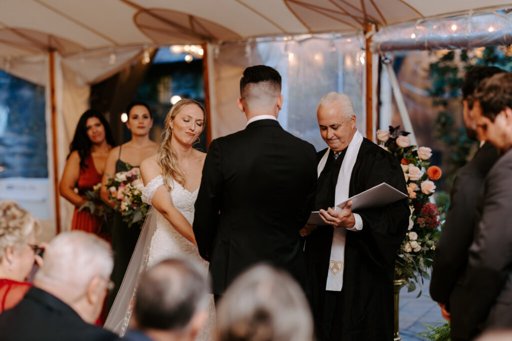 Bride and groom hold hands while bride smirks during their wedding ceremony at The Willowdale Estate in Topsfield, MA.