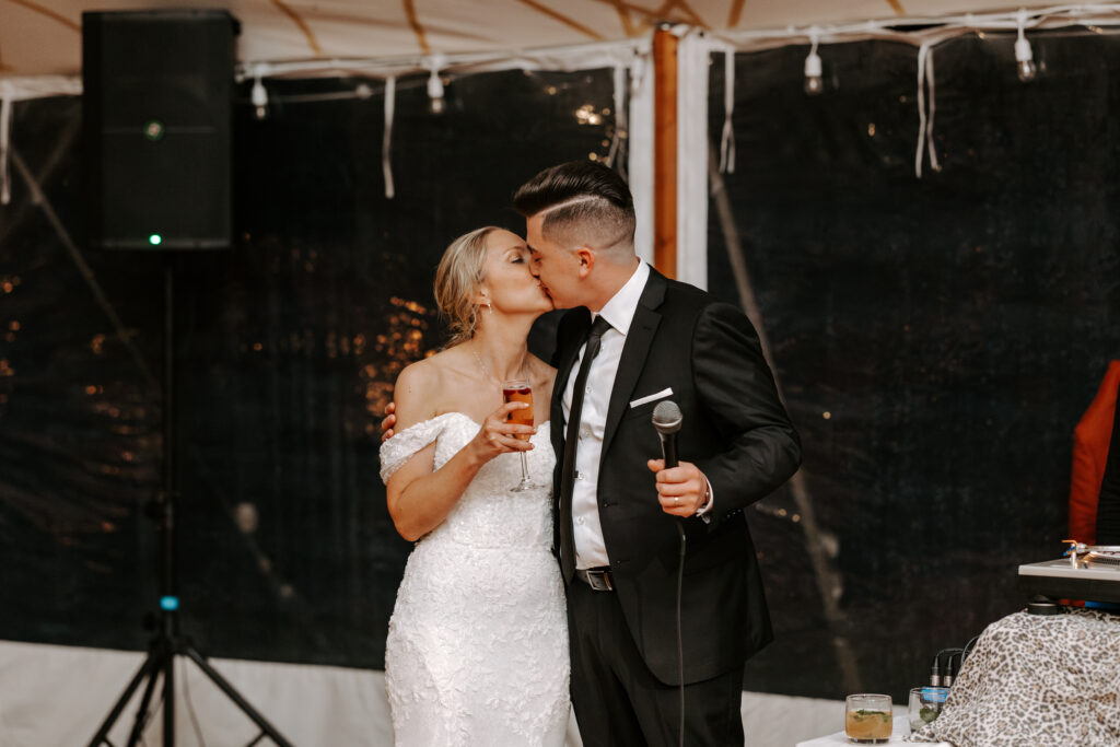 Bride and groom kiss while giving a welcome speech to guests at their wedding reception at The Willowdale Estate in Topsfield, Massachusetts.