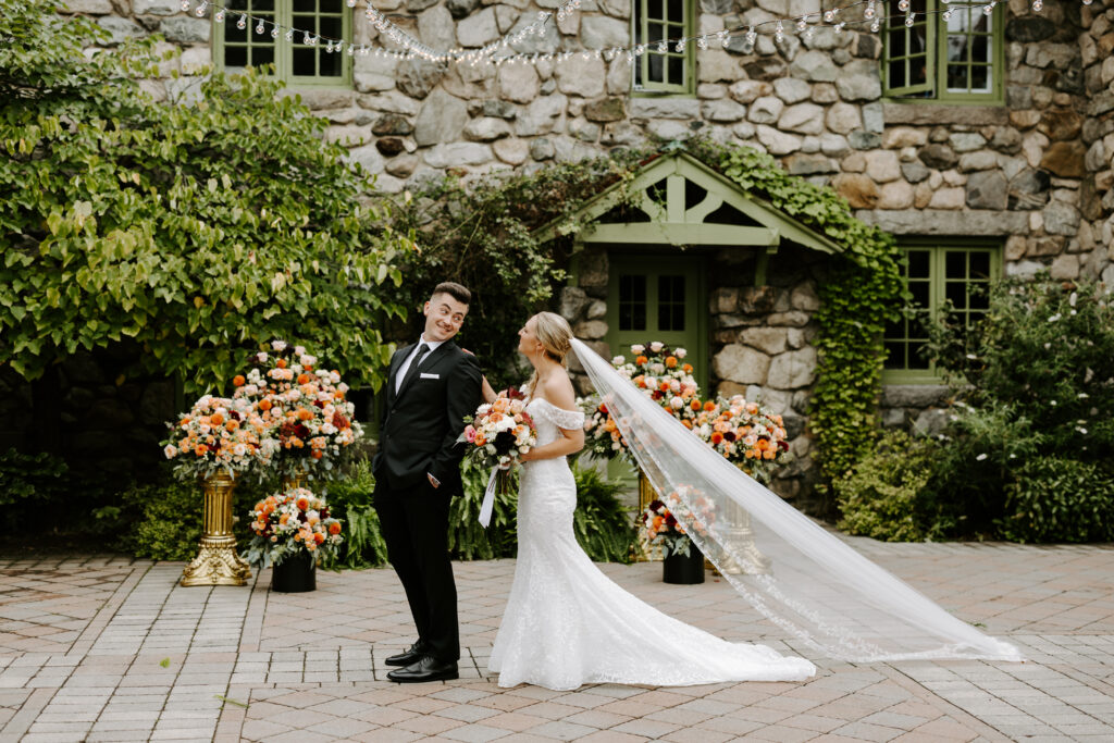 Groom looks over his shoulder at bride to reveal their first look in the courtyard at their wedding at The Willowdale Estate.