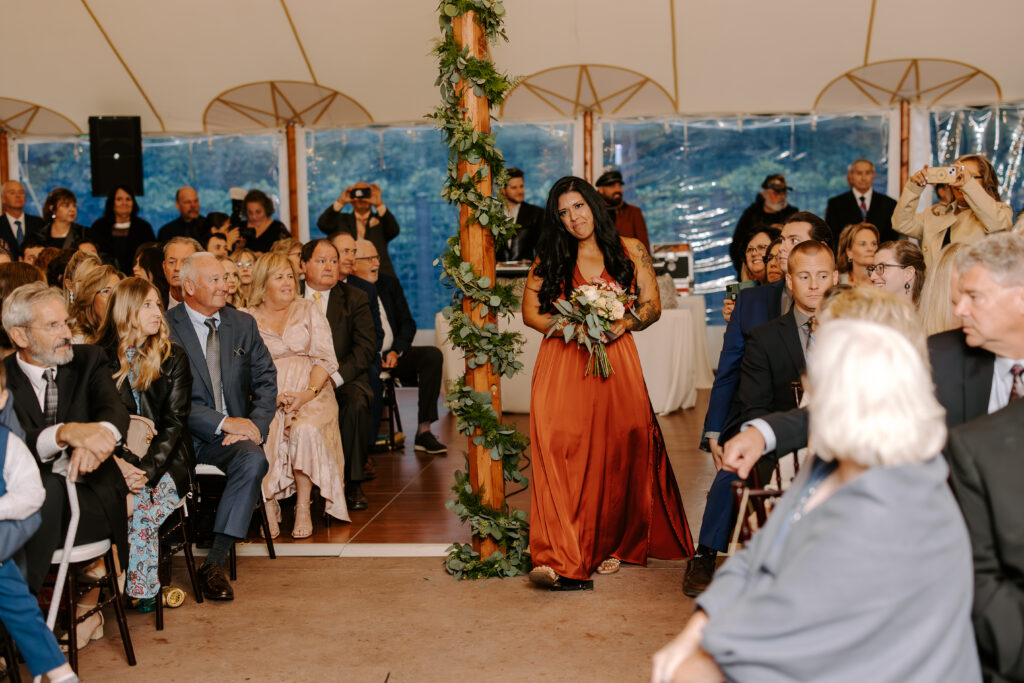 Bridesmaid walks down the aisle ahead of bride at a rainy fall wedding at The Willowdale Estate.