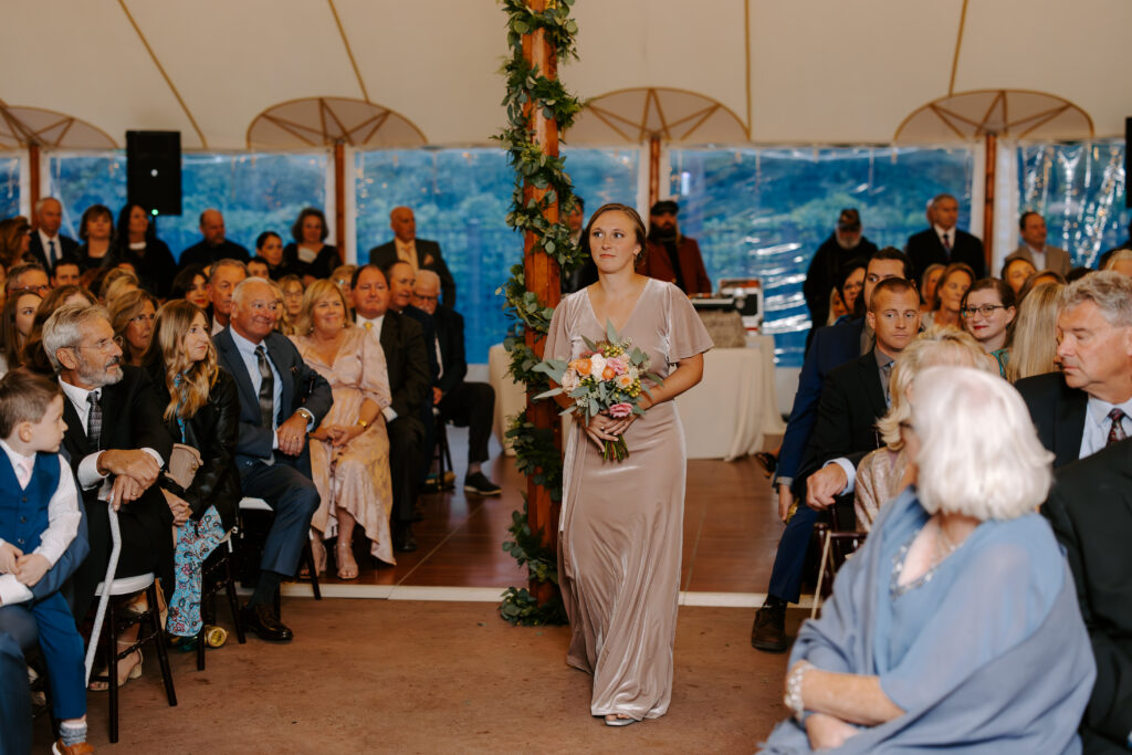 Bridesmaid walks down the aisle ahead of bride at a rainy fall wedding at The Willowdale Estate.