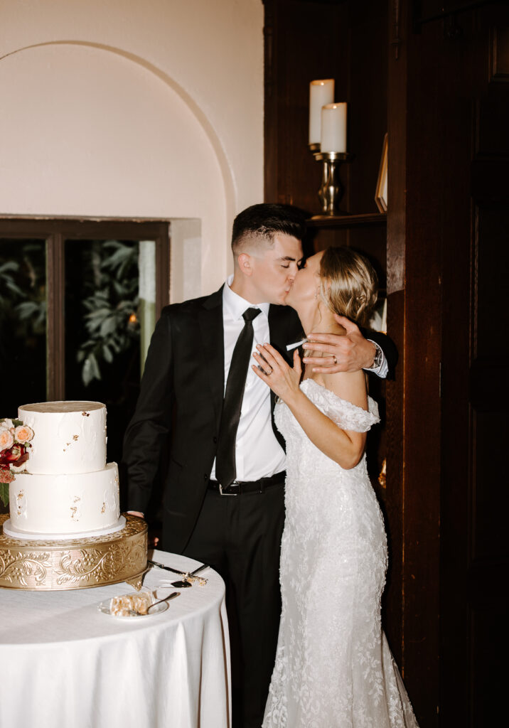 Bride and groom kiss and show off wedding bands after cutting their wedding cake inside at The Willowdale Estate.