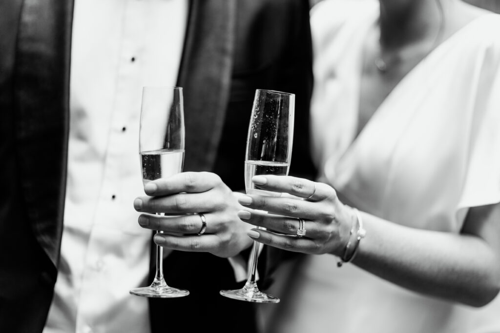 Bride and groom hold champagne glasses and show off wedding rings at SRV in Boston, Massachusetts