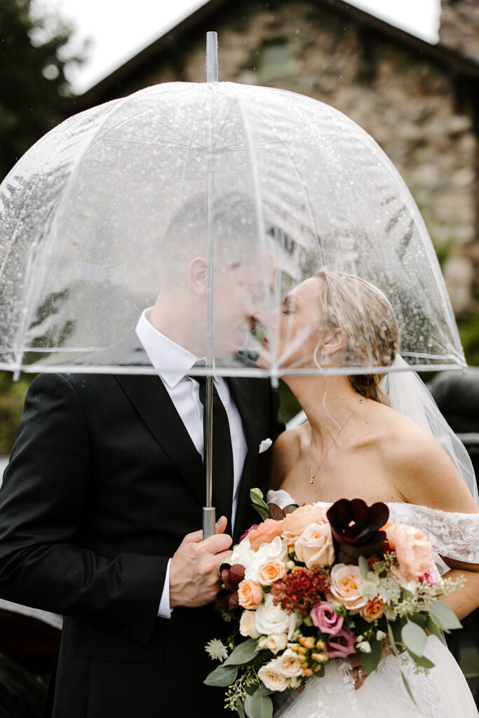 Bride and groom touch noses under umbrella on rainy wedding day at The Willowdale Estate