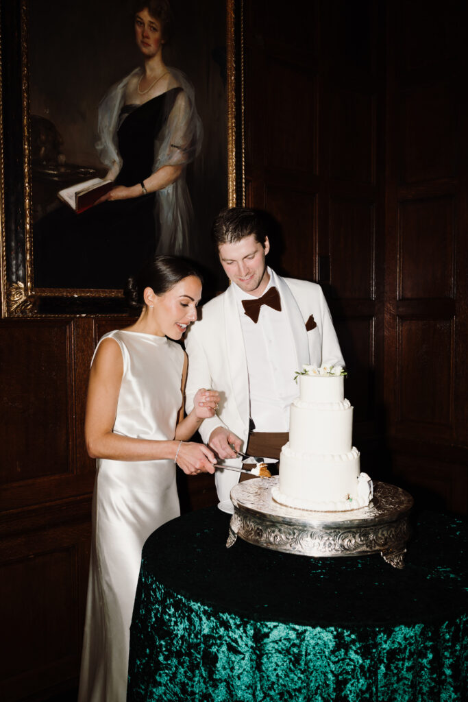 Bride and groom cut their cake during their indoor wedding reception at The Harvard Club of Boston.