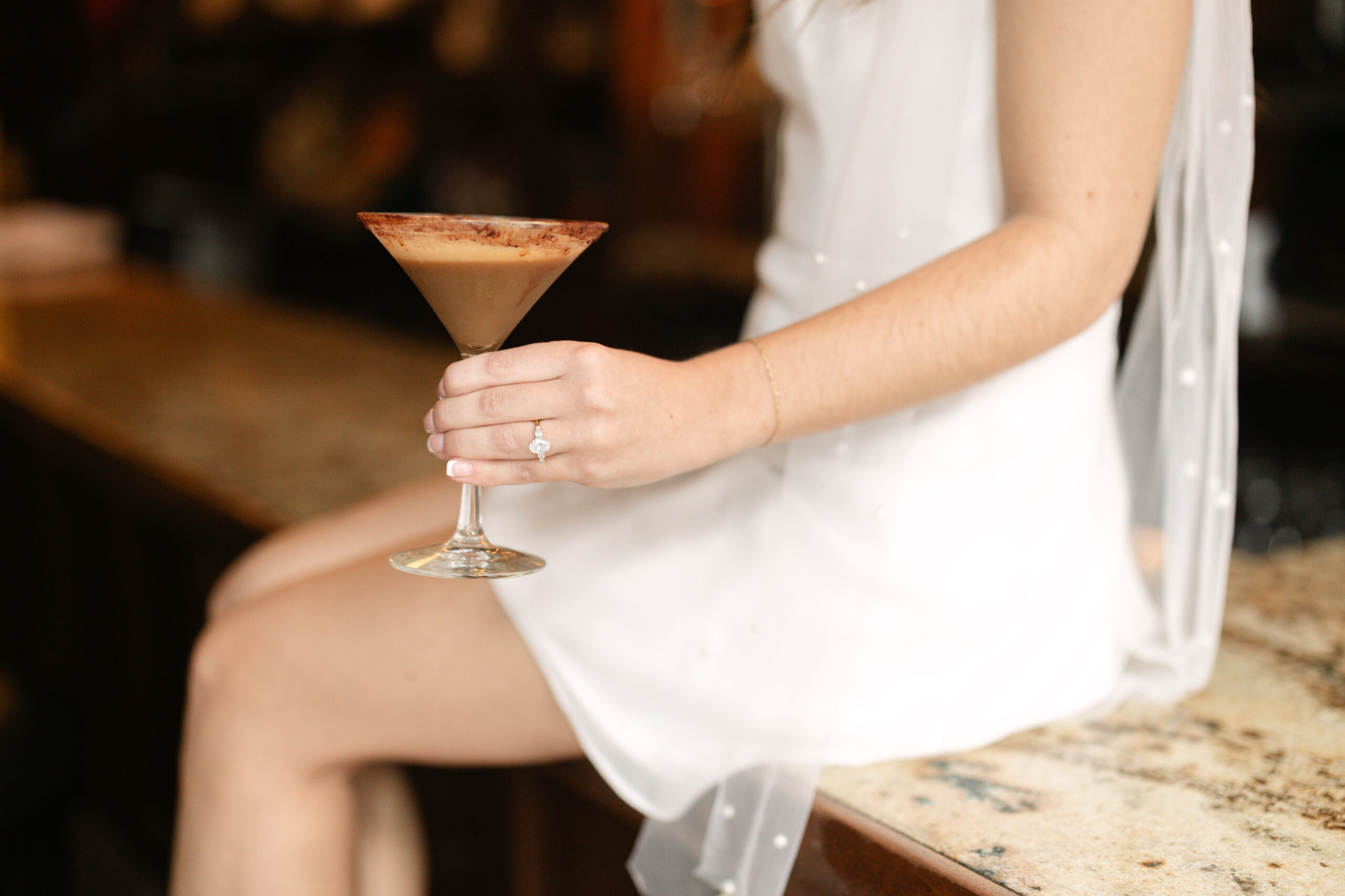 Bride holds espresso martini and shows engagement ring