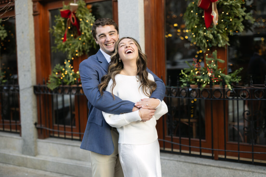 Groom hugs bride from behind and laughs during photo session in Boston