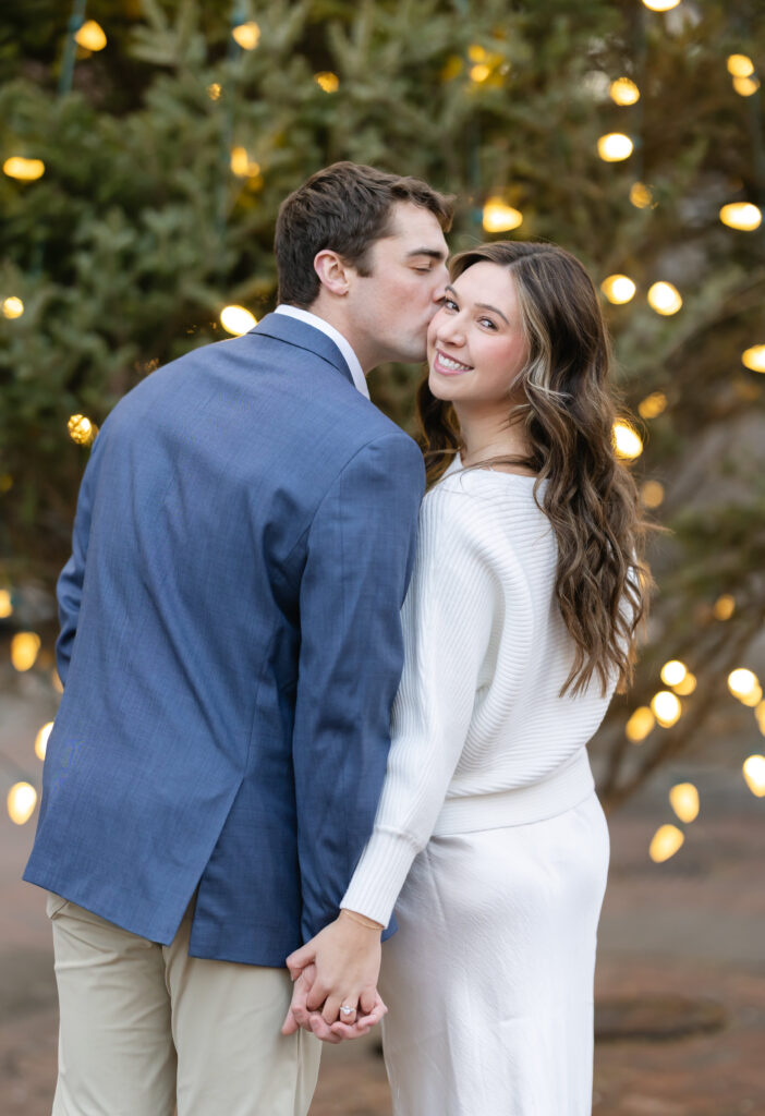 Groom kisses bride on the cheek in front of christmas tree in Boston