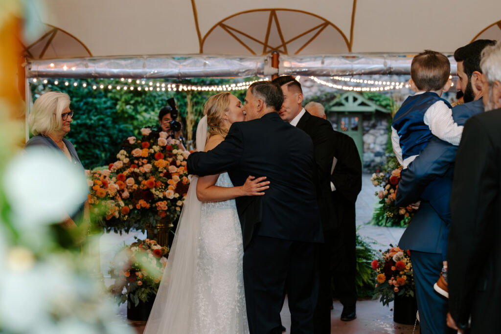 Bride and her father share a hug as he hands her off to her husband to be  during wedding ceremony at The Willowdale Estate in Topsfield, MA.