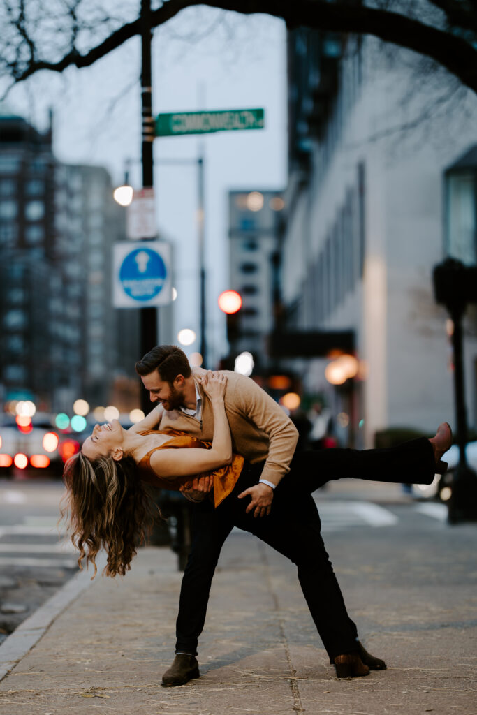 After planning an executing the perfect Boston proposal, Man dips his fiance in front of Commonwealth Ave sign in Boston, Massachusetts
