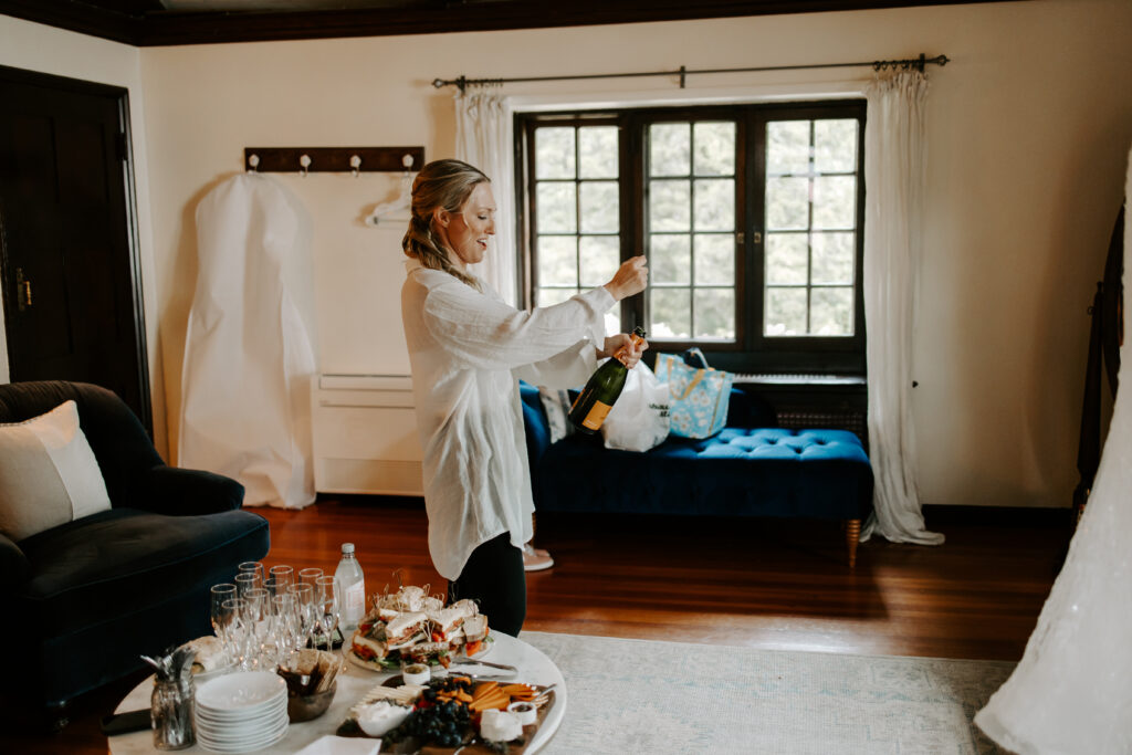 Bride pops a bottle of champagne as she is getting ready for her wedding at The Willowdale Estate.