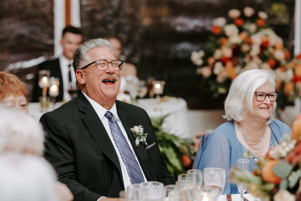Groom's mother and father laugh during toasts at rainy fall wedding at The Willowdale Estate in Topsfield, Massachusetts