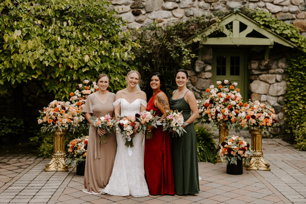 Bride and her 3 bridesmaids (bridal party) smile in front of The Willowdale Estate for her fall wedding.