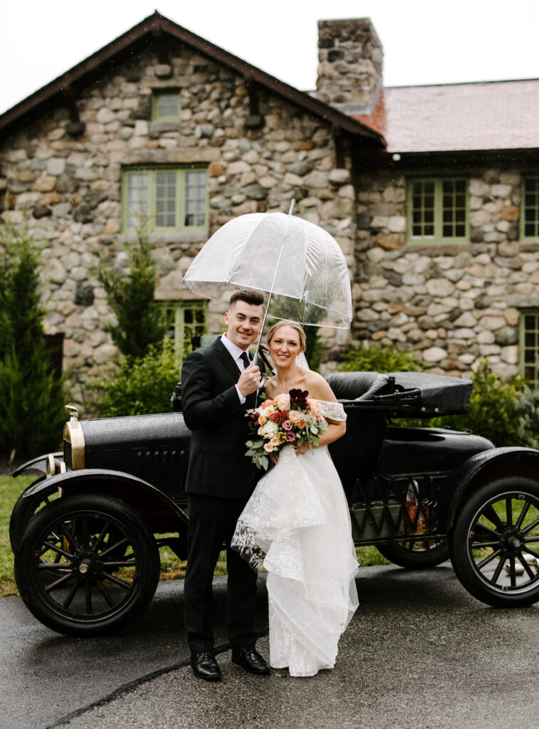 Bride and groom smile under an umbrella in front of The Willowdale Estate.