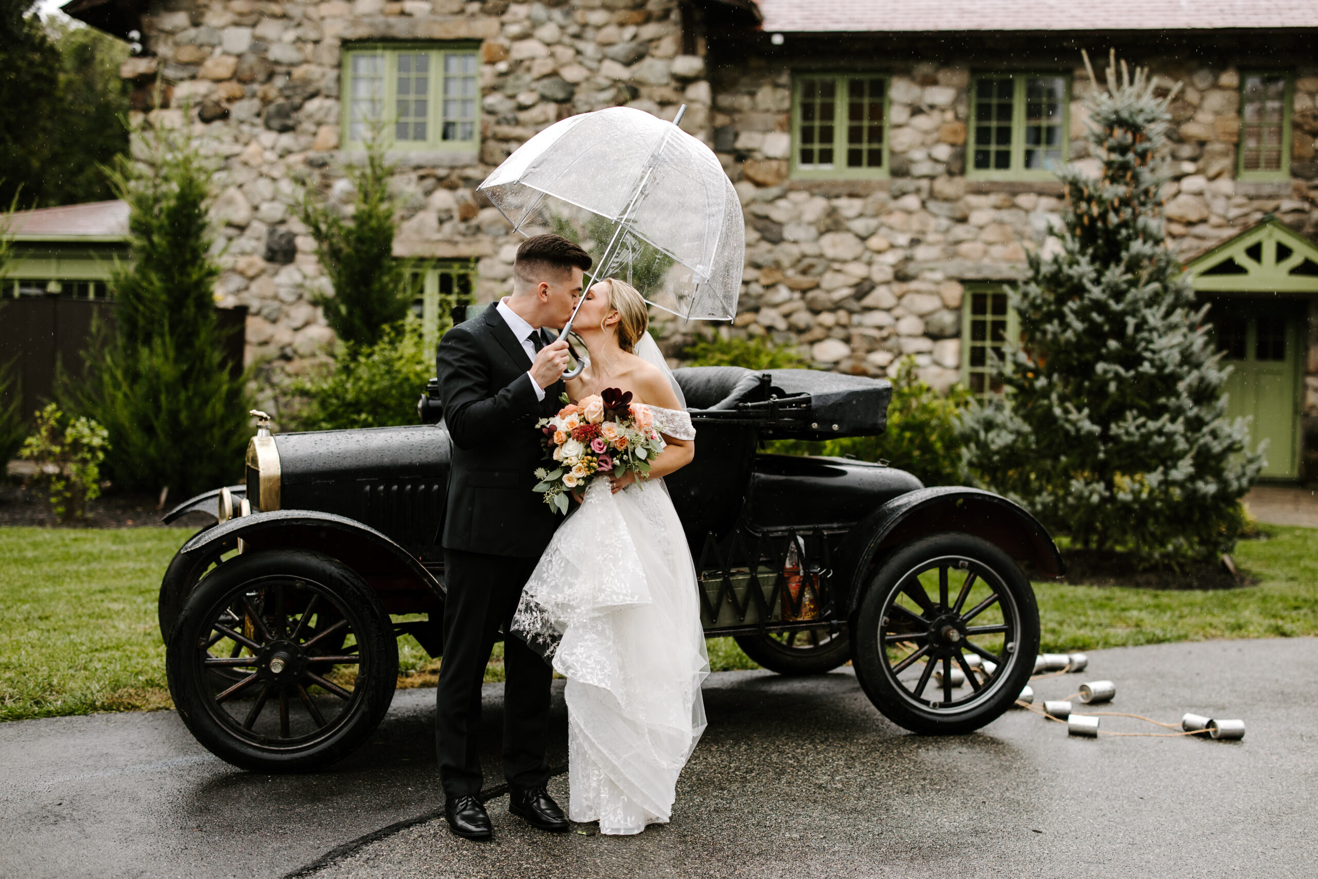 Bride and Groom kiss in front of vintage car during rainy wedding day at The Willowdale Estate