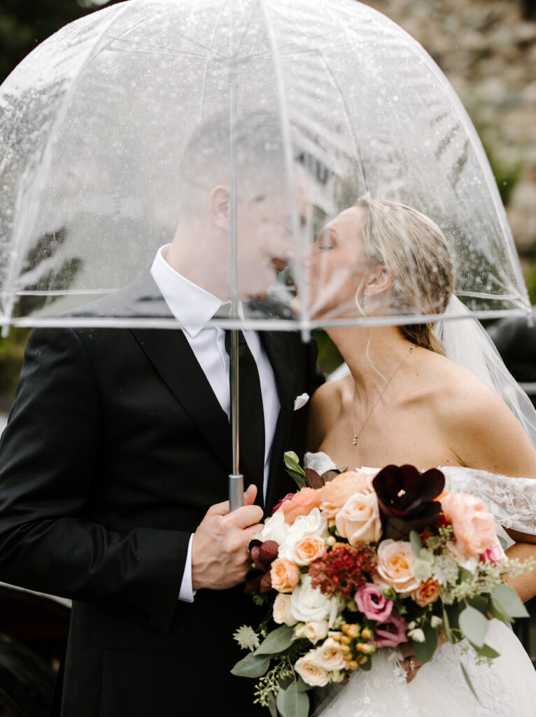 Bride and groom just barely kiss under an umbrella in front of The Willowdale Estate.