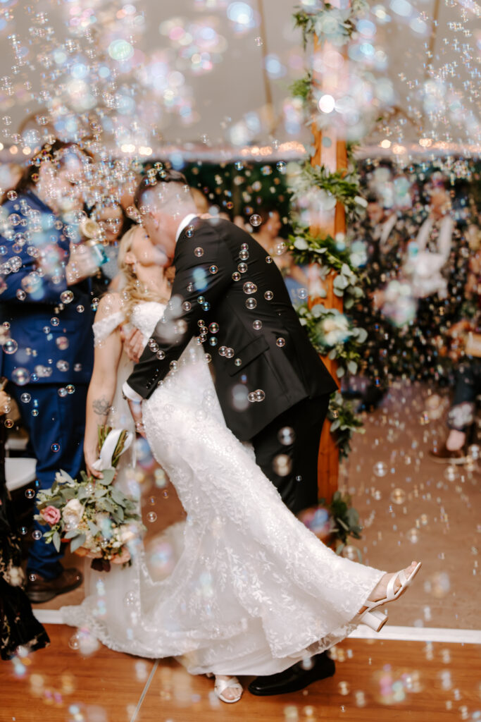 Bride and groom kiss while bubbles surround them during their tented wedding ceremony at The Willowdale Estate.