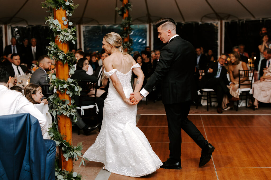 Bride and groom exit the dance floor after giving a welcome speech to guests at their rainy fall wedding at The Willowdale Estate in Topsfield, Massachusetts.