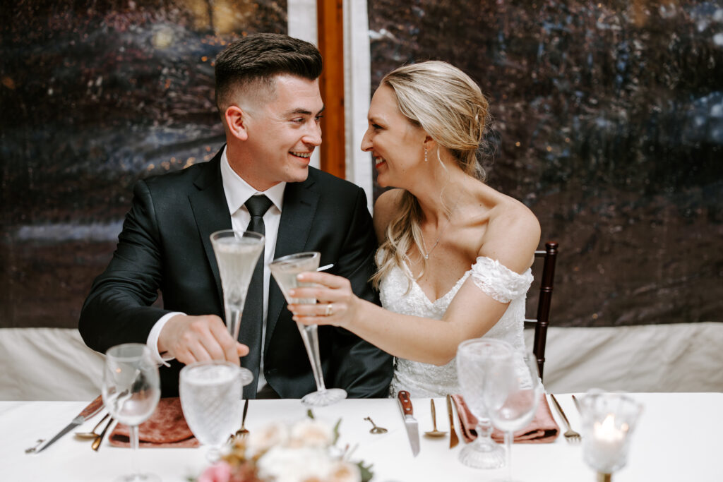 Bride and groom smile at each other while raising their glasses for a toast at their fall wedding at The Willowdale Estate.