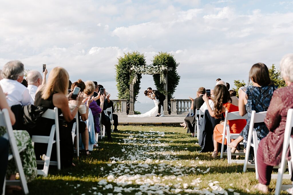 Bride and groom share first kiss at wedding ceremony at Castle Hill Inn, Newport, RI. Learn the essential wedding planning steps for newly engaged couples.