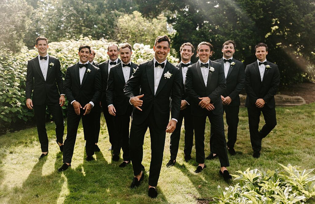 Groom and groomsmen walk toward camera in gardens at Castle Hill Inn Newport, RI