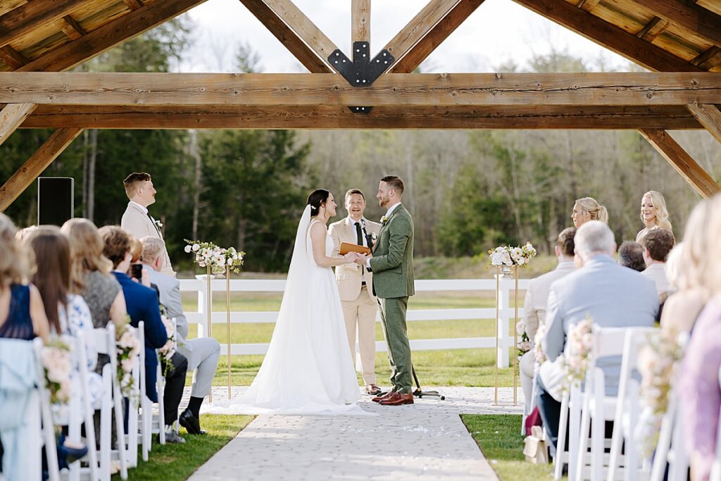 Outdoor wedding ceremony, bride and groom laugh at The Barn at Bull Meadow in Concord, New Hampshire.