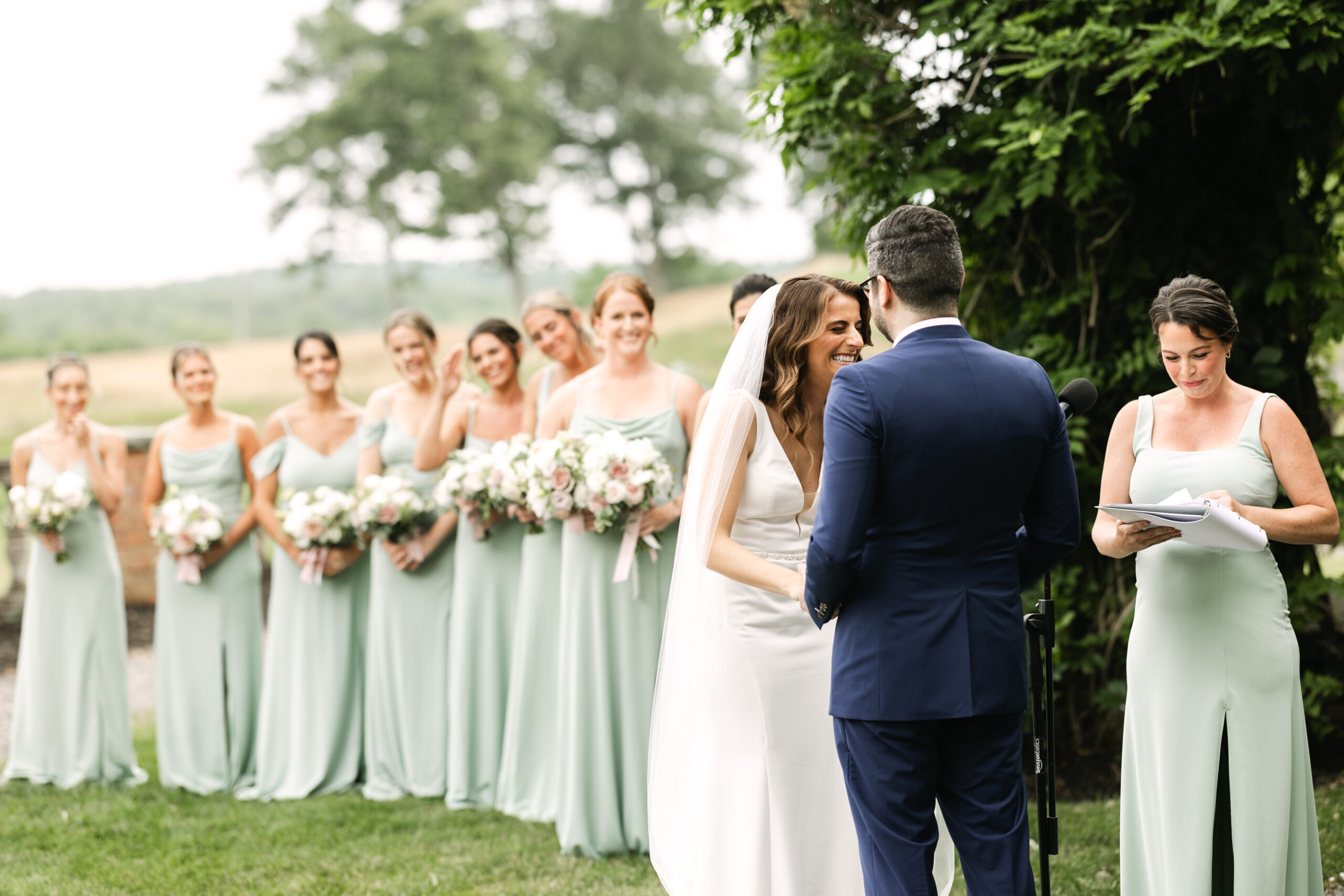 Bride and groom laugh during boston wedding ceremony alongside bridesmaids in green dresses.