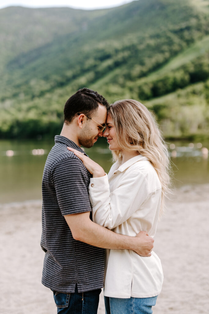 Bride and groom hold each other and nuzzle close during summer engagement session in the mountains of New Hampshire.
