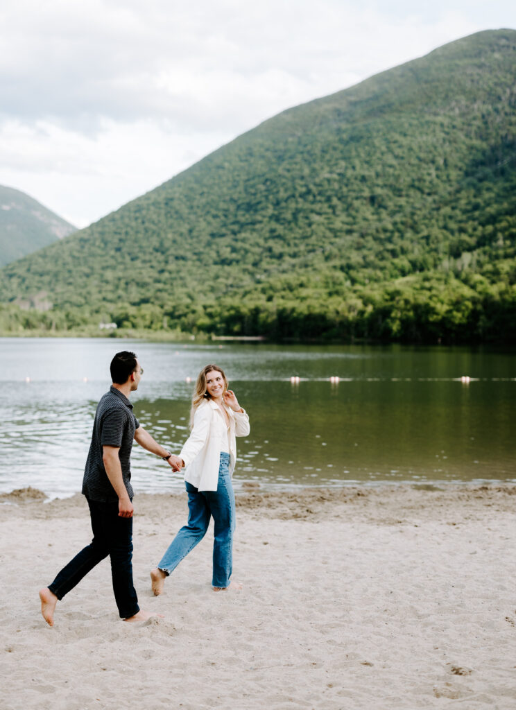 Bride and groom hold hands and walk across Echo Lake Beach in New Hampshire.
