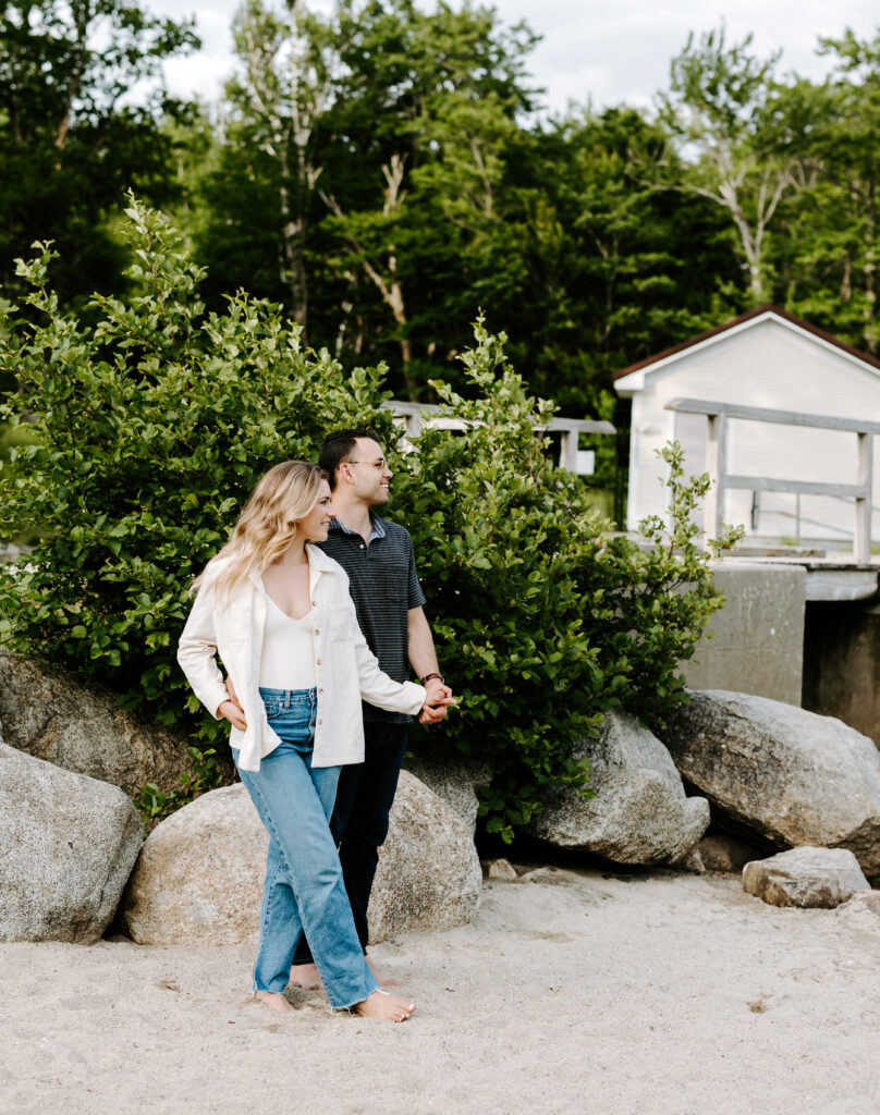 Bride and groom hold hands and smile during summer mountain engagement photo session in New Hampshire.