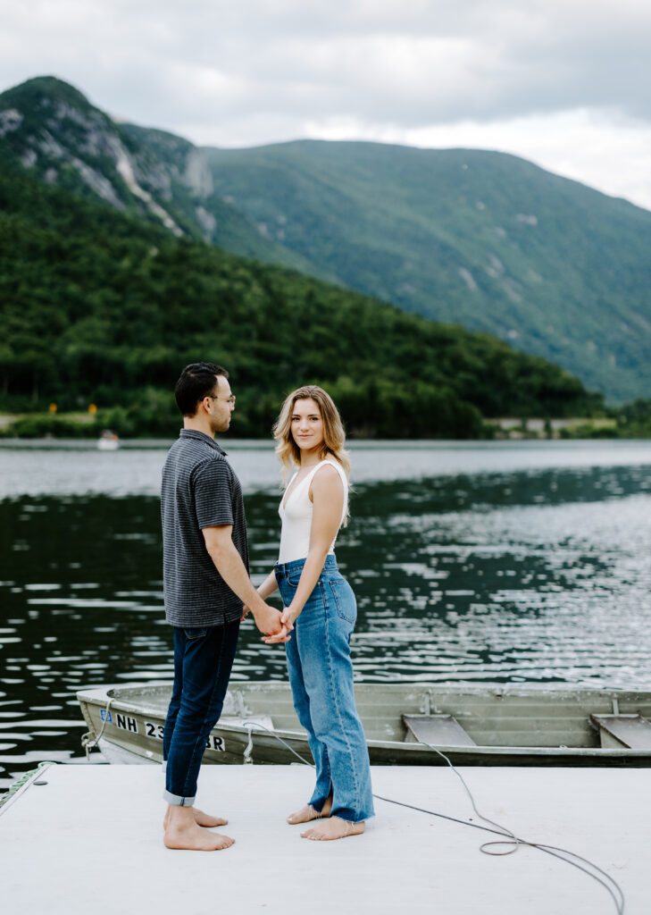 Groom holds hand with bride and looks at her on boat dock in NH during engagement photos.