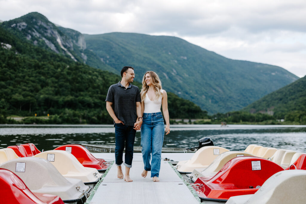 Couple holds hands and looks at each other during NH engagement photo session in the mountains.