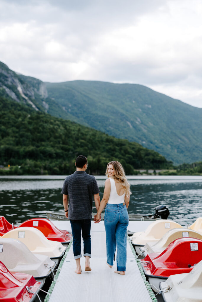 Bride holds grooms hand and smiles over shoulder during NH mountain engagement photo session
