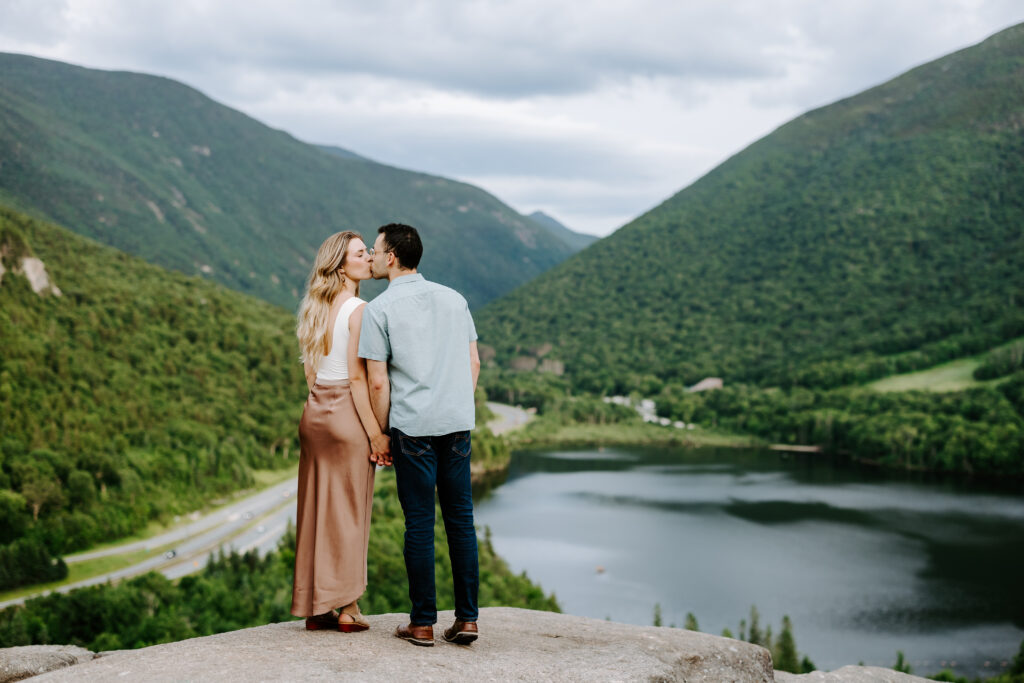 Couple kisses at top of Artists Bluff lookout in NH at engagement photo session
