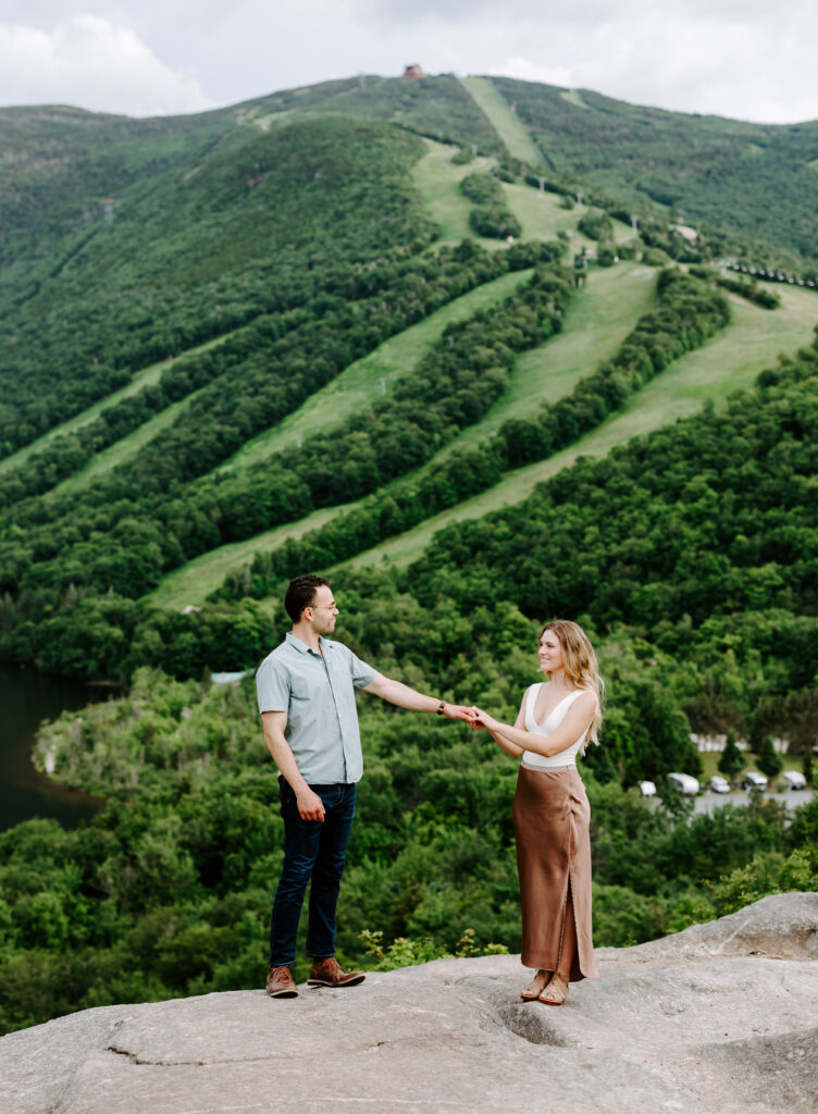 Bride and groom smile at each other in front of Cannon Ski Mountain in New Hampshire during summer mountain engagement photos in New Hampshire
