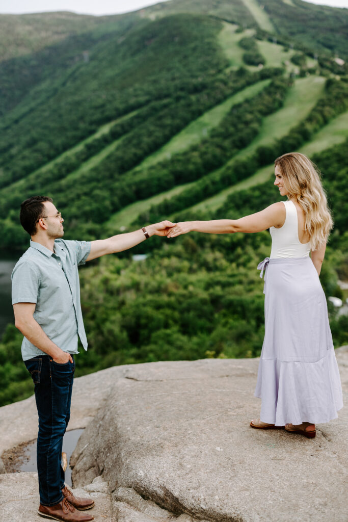 Bride and groom hold one hand on top of NH white mountains during summer mountain engagement photos in New Hampshire
