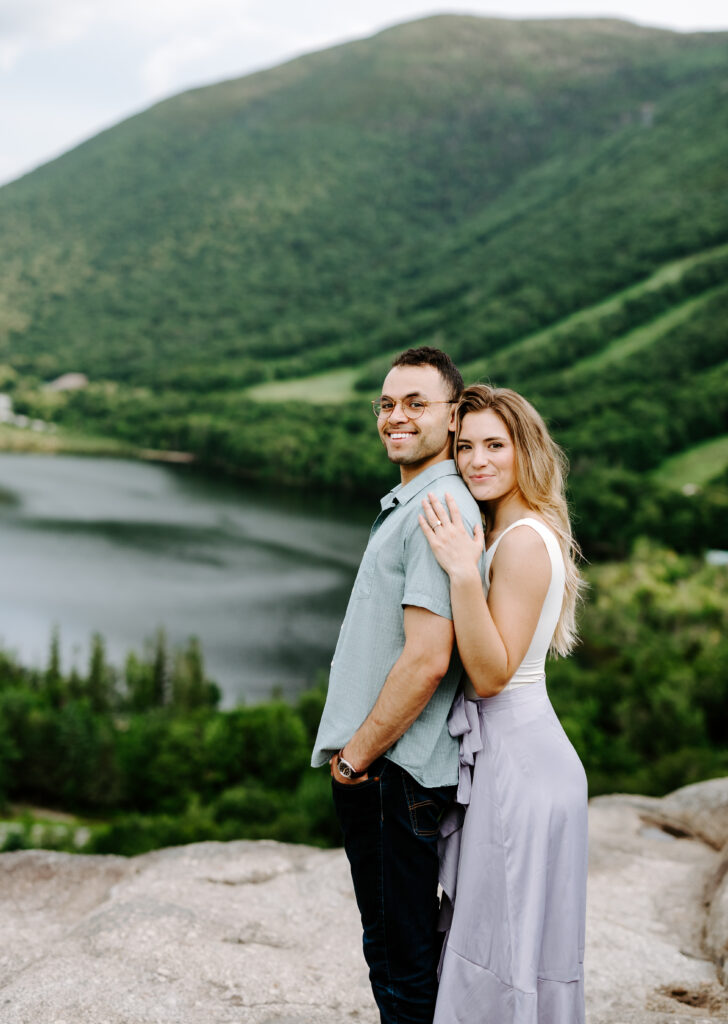 Bride and groom smile at NH wedding photographer in summer mountain engagement photos in New Hampshire