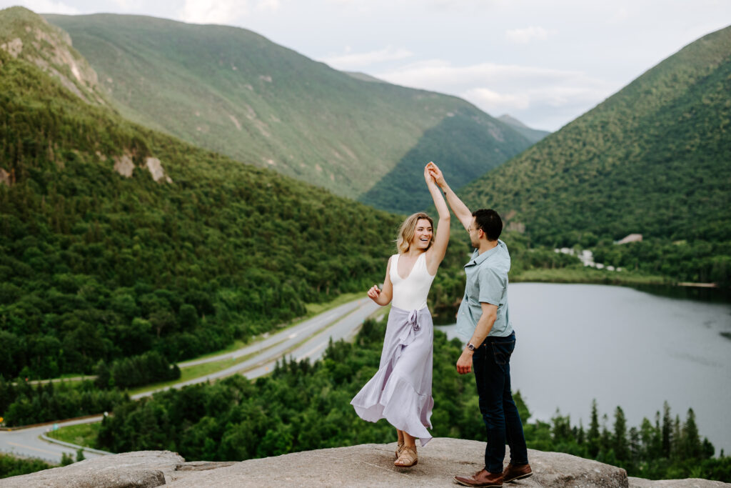 Couple dances on top of NH white mountains during summer mountain engagement photos in New Hampshire