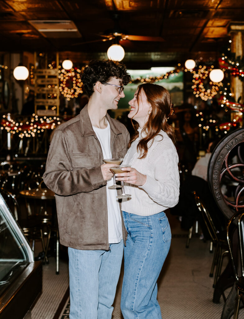 Couple smiles at each other before kissing with espresso martinis in boston cafe