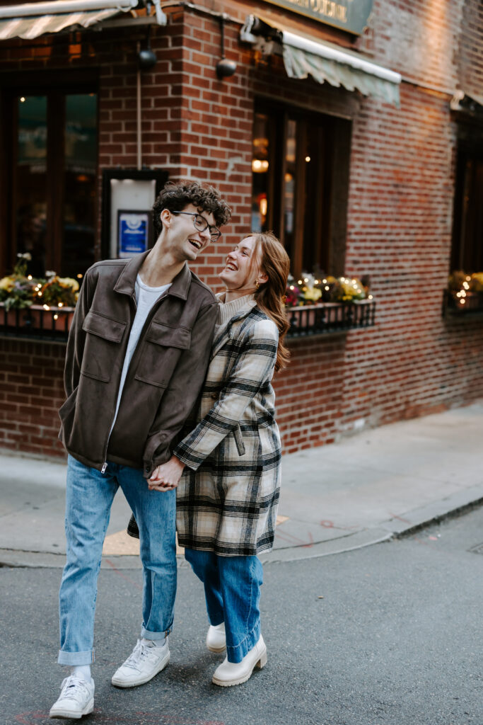 Couple walks across the street while laughing in boston photos