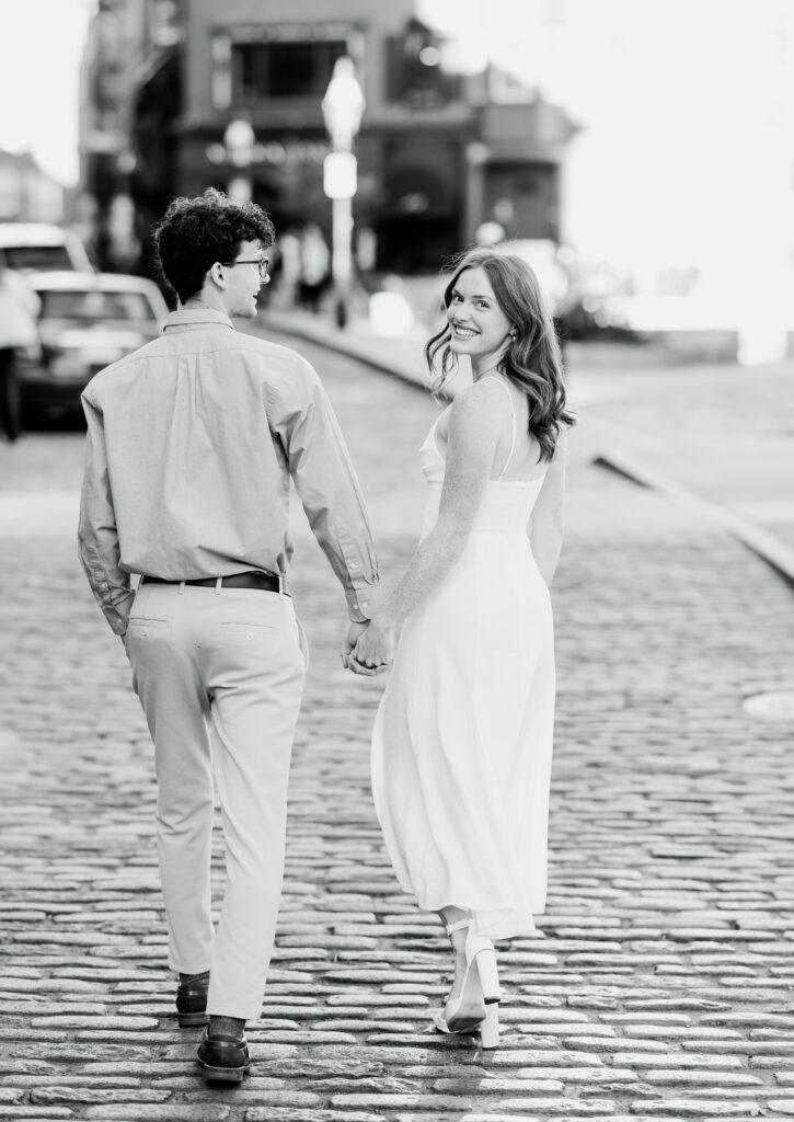 Bride smiles over shoulder while holding hands and walking down the street in the north end of boston