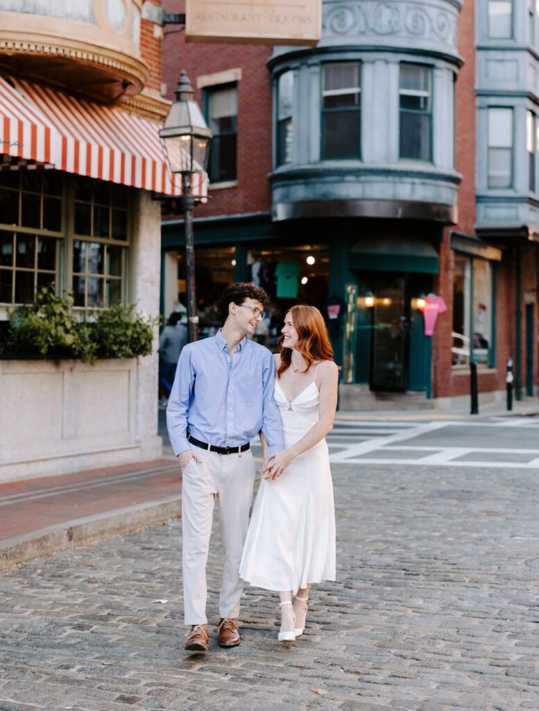 Couple walks towards the camera while smiling in Boston engagement photo session in the North end