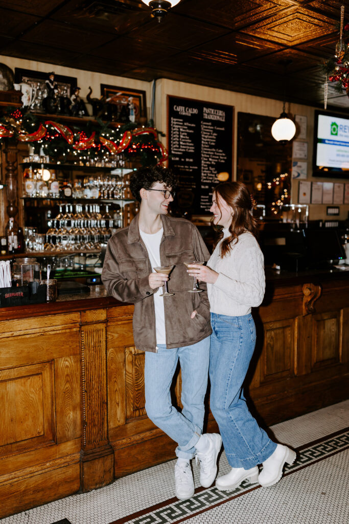 Couple stands at boston bar with espresso martinis and smiles at each other